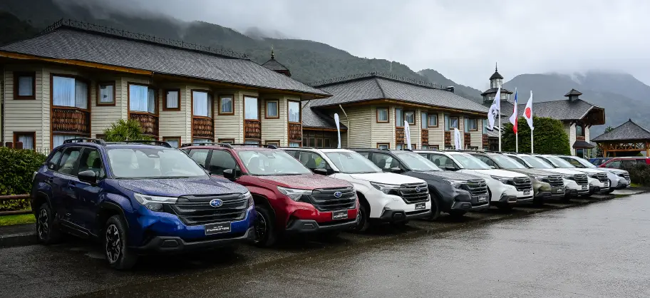 Modelos Subaru estacionados en parqueadero con casas de condominio y montañas de fondo.