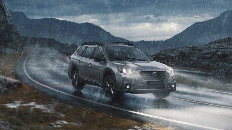 Auto Subaru Outback en carretera con clima lluvioso y montañas de fondo