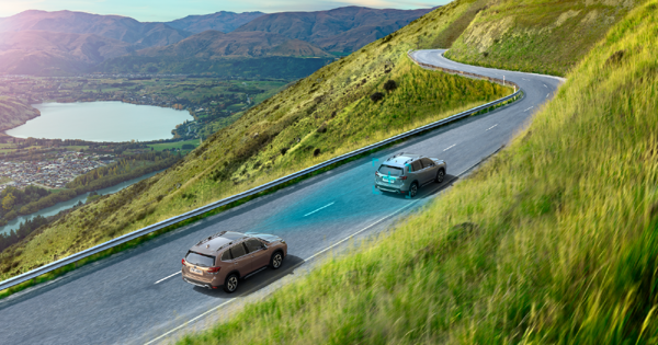 Autos Subaru en carretera rural en montaña y lago de fondo