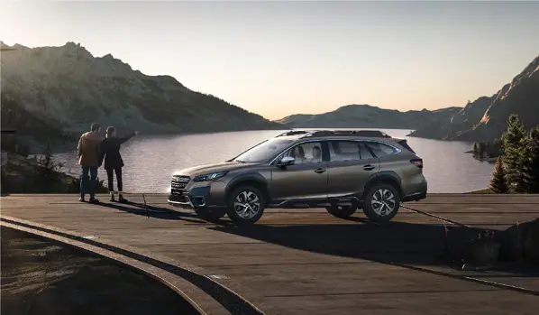 pareja junto a lago con montañas de fondo y auto Subaru