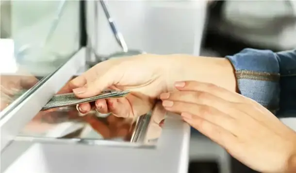 Manos de mujer pasando sus documentos a través de una ventanilla