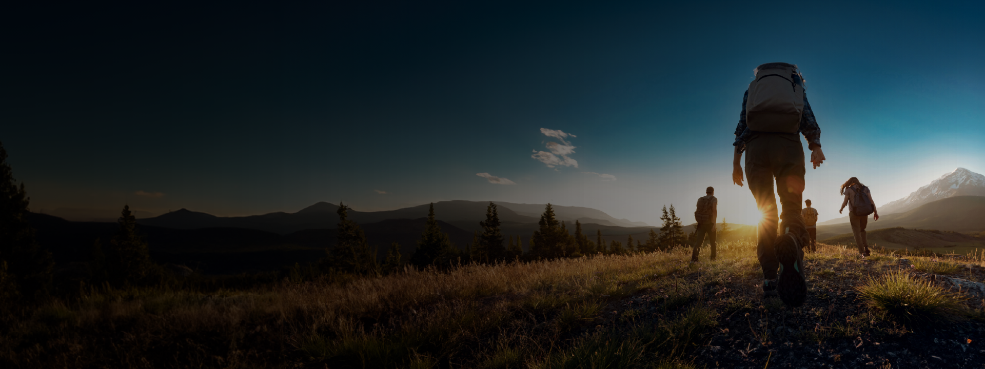 Personas haciendo senderismo en montaña con amanecer y montañas de fondo.