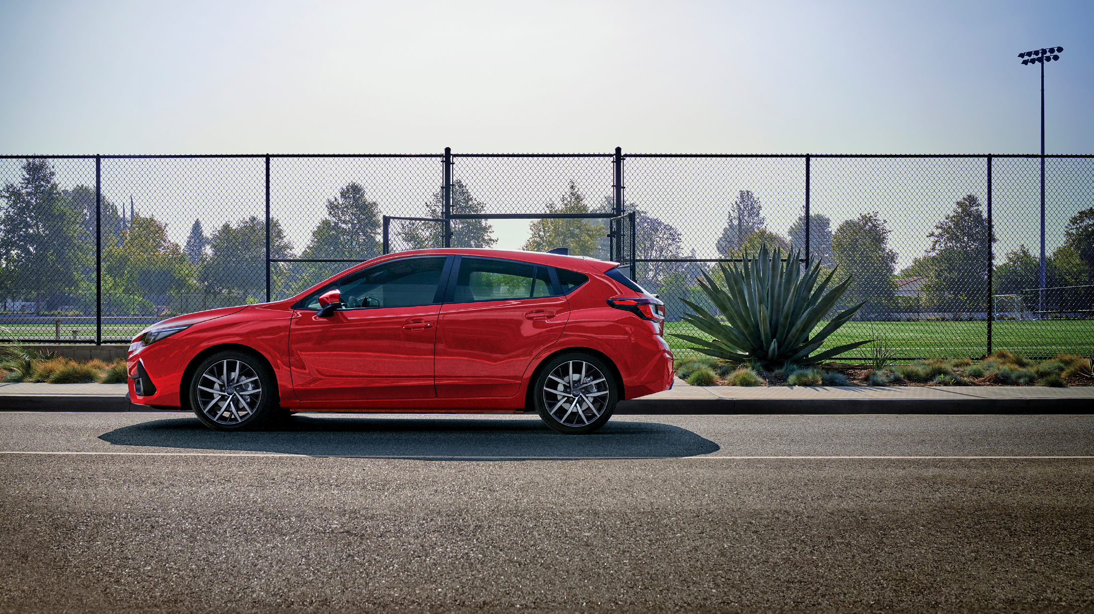 Auto Subaru color rojo aparcado frente a parque 