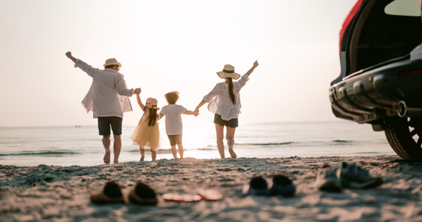 Familia feliz en la playa con auto Subaru parqueado junto a ellos