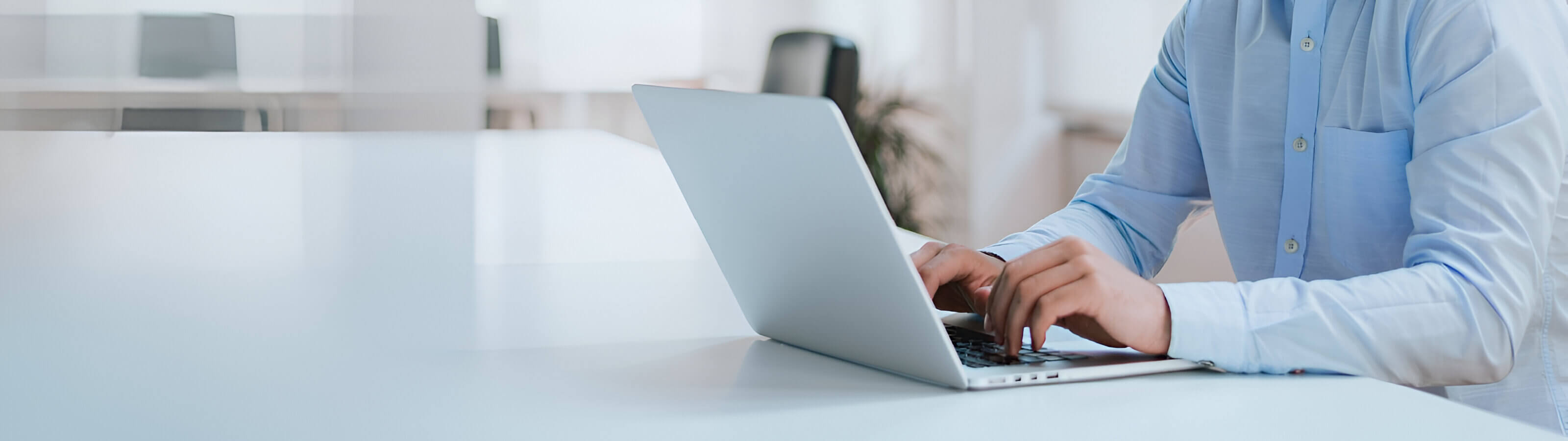Hombre con camisa elegante consultando su computador sobre escritorio blanco