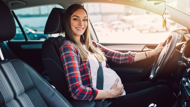 mujer embarazada sonriente en el asiento de conductor utilizando cinturón de seguridad