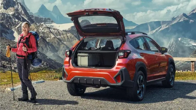 Auto Subaru color rojo con vista a montaña y señora sonriente con implementos de caminata