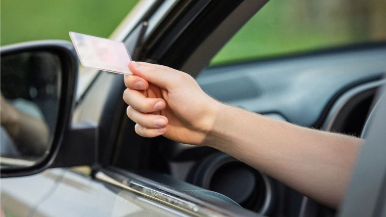 Persona mostrando su licencia de conducción desde la ventana del piloto